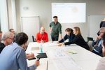 In diesem Workshop sitzt eine Gruppe Menschen um einen Tisch und erarbeitet Inhalte in entspannter Atmosphäre. 